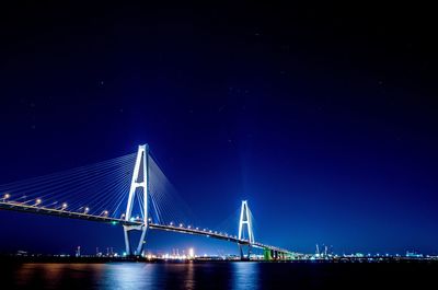 Illuminated suspension bridge over river against sky at night