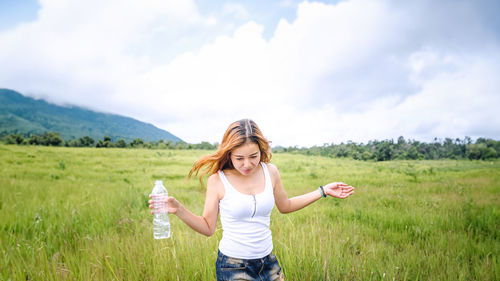 Young woman with arms raised standing on field against sky