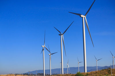 Low angle view of wind turbines on field against clear blue sky