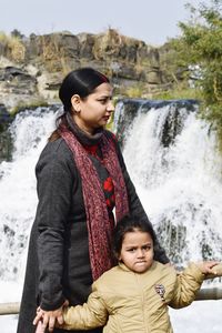 A young woman with her daughter standing near to a waterfall