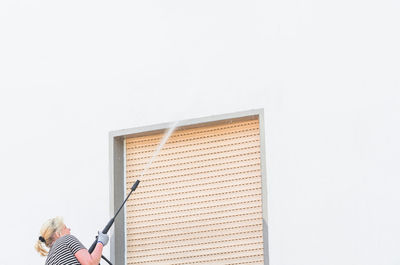 Low angle view of woman spraying water on wall