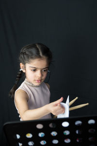 Girl playing drum while standing against curtain