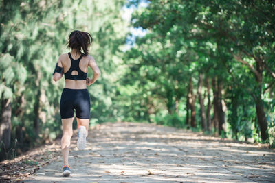 Full length rear view of young woman jogging on road amidst trees