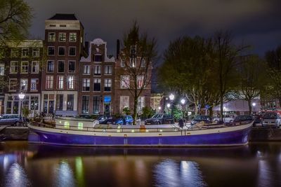 Boat moored in river against illuminated buildings at city