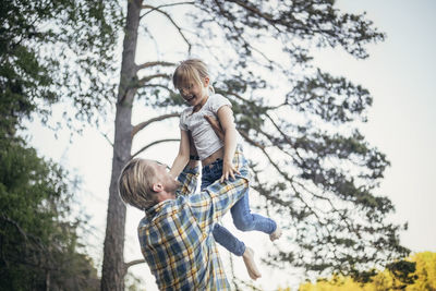 Happy father holding daughter in air against trees
