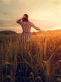 Rear view of woman standing at wheat field during sunset