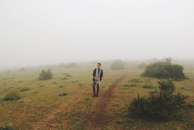 Young woman standing on grassy field during foggy weather