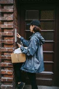 Side view of female courier delivery person ringing doorbell while arriving at doorstep