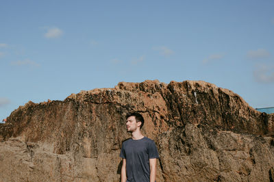 Low angle view of young woman standing on rock against sky