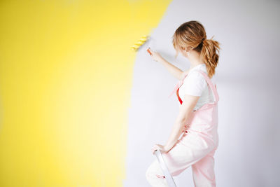 Side view of woman standing against yellow background