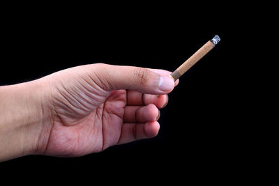 Close-up of hand holding cigarette over black background