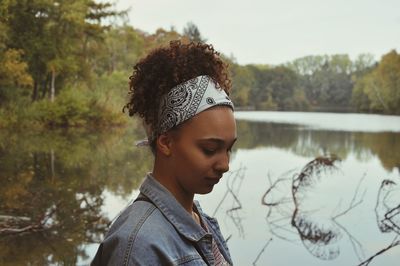 Side view of teenage girl standing against lake in forest