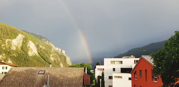 Rainbow over buildings and mountains against sky