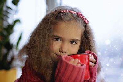 Portrait of smiling girl holding coffee cup sitting by window