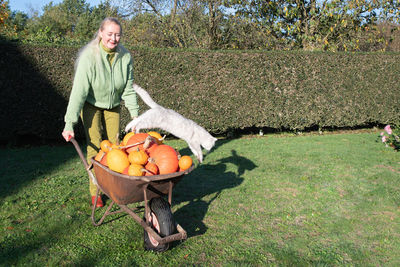 Middle-aged blonde woman at a large cart with ripe pumpkins and a small kitten