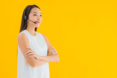 Beautiful young woman standing against yellow background