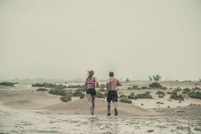 Rear view of people walking on beach against clear sky