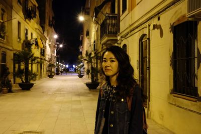 Woman standing on illuminated street amidst buildings at night