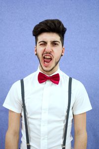 Portrait of young man wearing bow tie against blue background