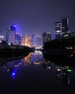 Illuminated buildings by river against sky in city at night