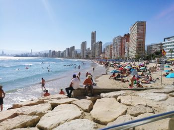 People on beach by city against clear sky