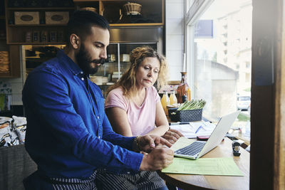 Colleagues with laptop and documents working at table in deli