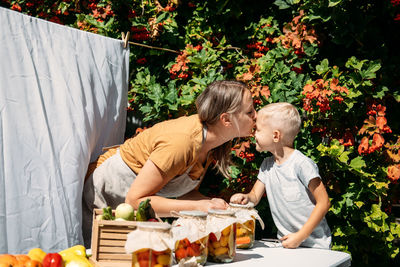 Happy family mother and son kid canning vegetables in the garden in summer day. canning and