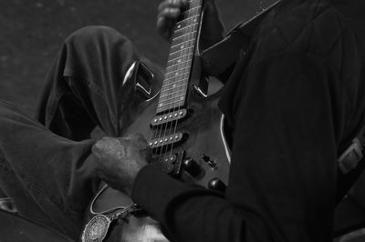 Midsection of street musician plying guitar at dusk