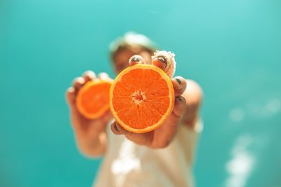 Low angle view of woman holding orange slices while standing against blue sky