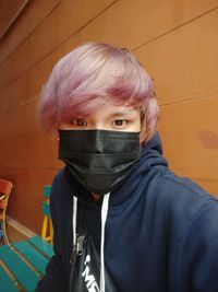 Portrait of young man with dyed hair wearing mask against wall