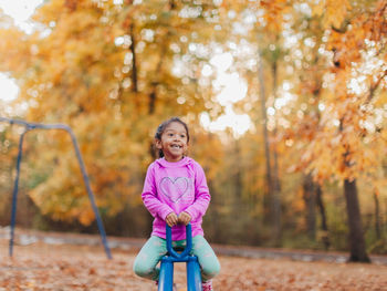 Full length of smiling girl standing against trees during autumn
