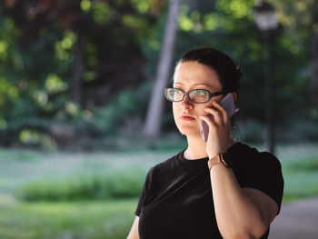 Caucasian woman in glasses emotionally talking on a mobile phone waving her hand in a public park