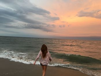 Rear view of woman standing on beach against sky