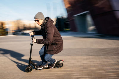 Side view of man riding push scooter on footpath in city