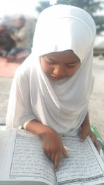Girl reading koran while sitting outdoors