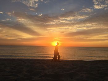 Silhouette woman and daughter walking on shore during sunset