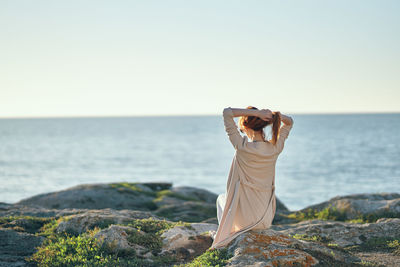 Person on rock by sea against clear sky