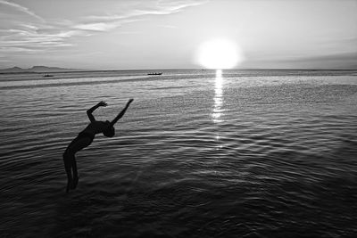 Silhouette boy jumping at sea against sky during sunset