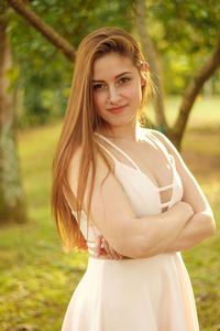 Portrait of beautiful woman with arms crossed standing on field at park