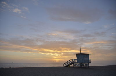 Lifeguard hut on sea shore against sky during sunset