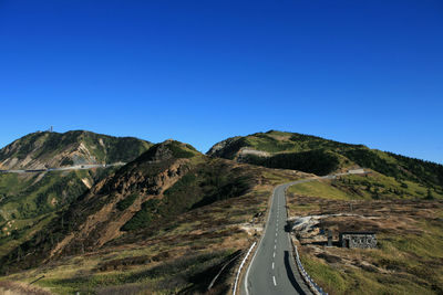 Road leading towards mountain against clear blue sky