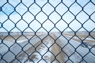 Highway against sky seen from chainlink fence