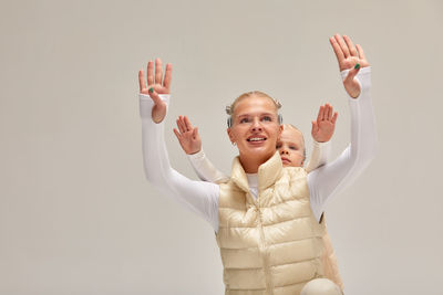 Portrait of smiling woman with arms raised standing against wall