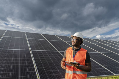 Thoughtful engineer with tablet pc standing in front of solar panels