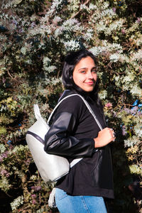 Portrait of smiling young woman standing against trees