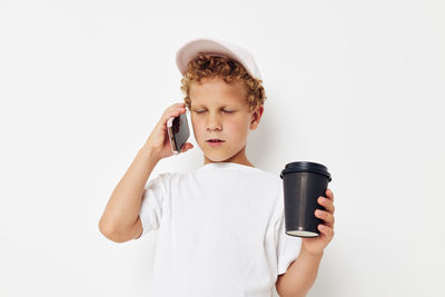 Boy holding coffee cup talking on phone against white background