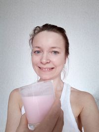 Portrait of smiling woman holding drink against wall