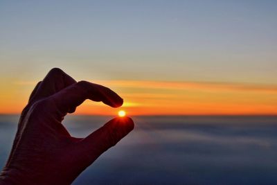 Hand holding sun over sea during sunset