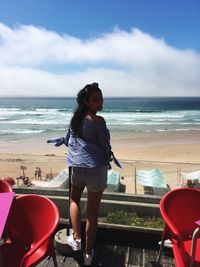 Young woman standing on beach against sky