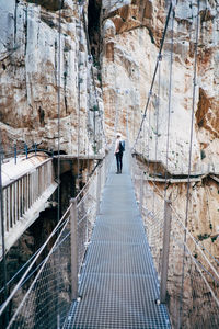 Rear view of young woman standing on rope bridge against rock